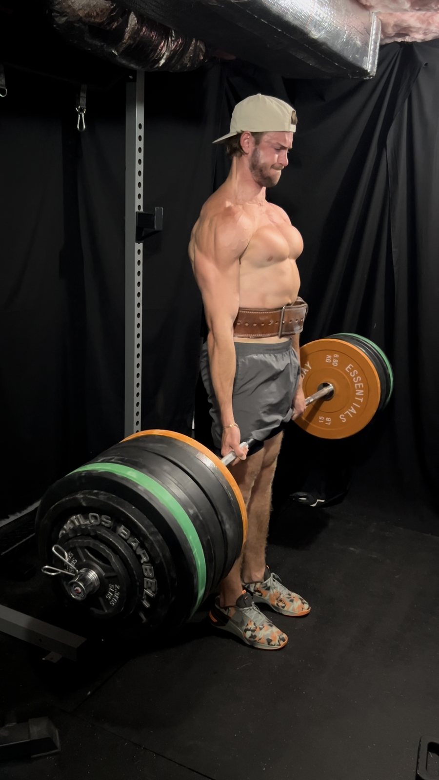 McKinley Slade at the top of a deadlift, side on, lifting belt fastened, loaded barbell against a black backdrop